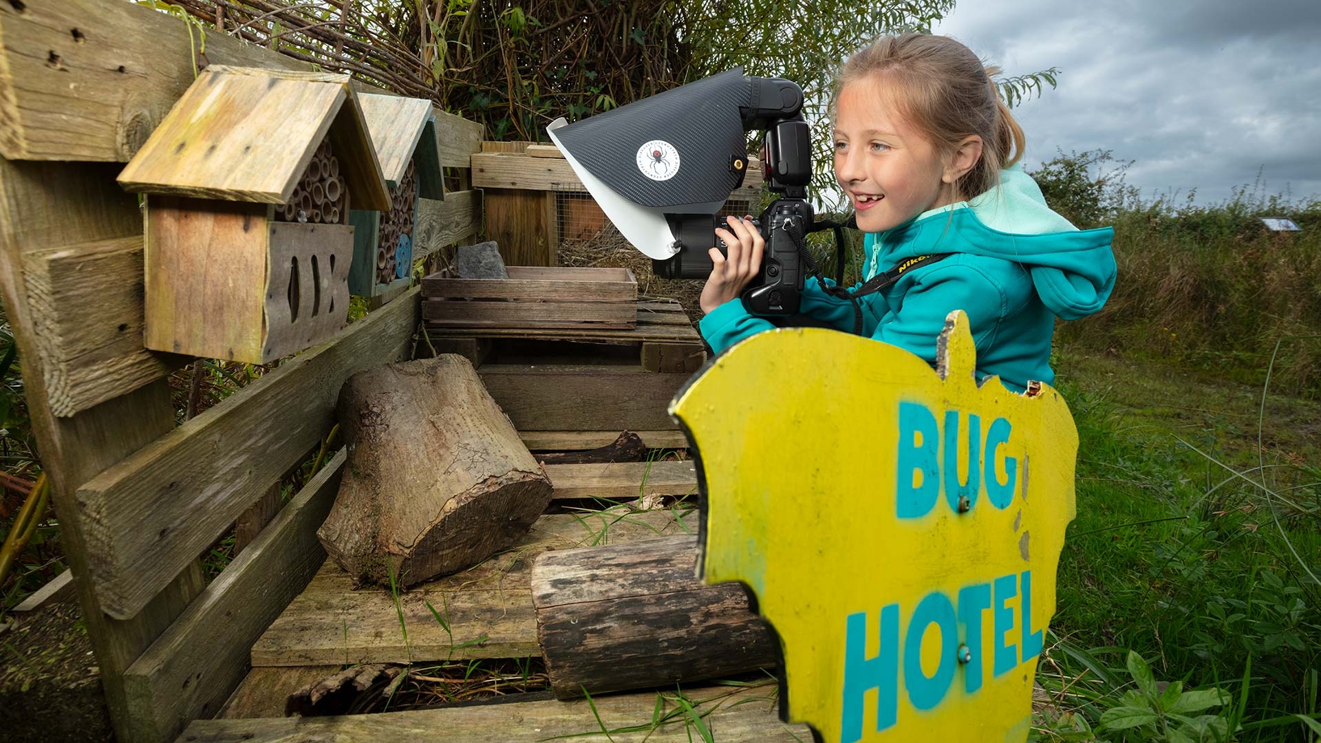 A girl points a camera at a bug hotel